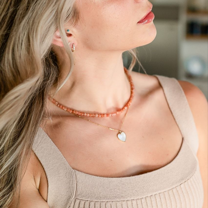 Woman wearing a necklace with a heart pendant in an indoor setting and summer beaded necklace 