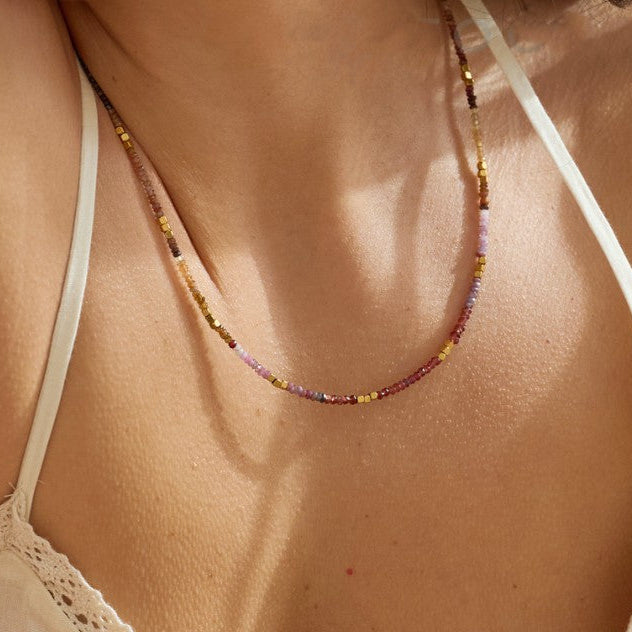 A close-up of a model wearing a delicate beaded sapphire necklace of fall colored sapphires waterproof gold 