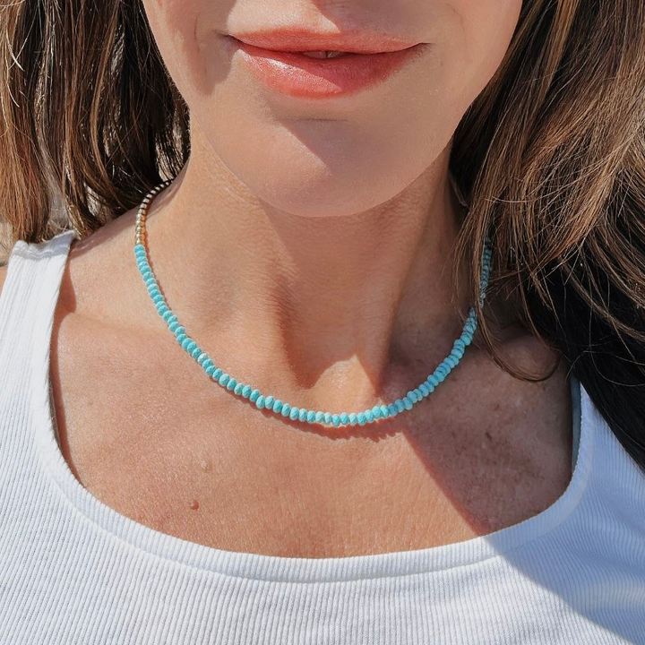 Close-up of a person wearing a turquoise beaded necklace against a neutral background