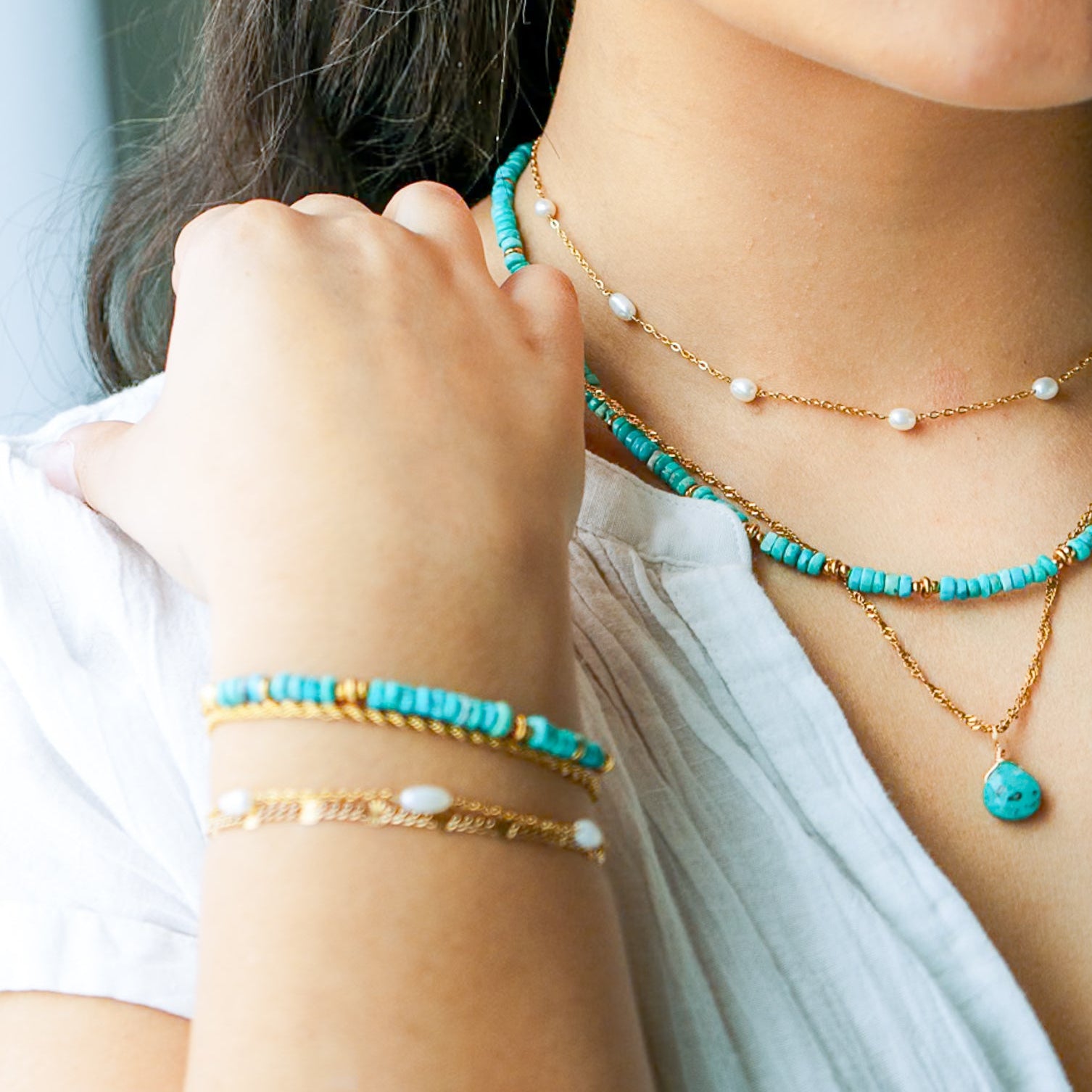 Close-up of a person wearing multiple necklaces, bracelets, and earrings with turquoise and gold colors.