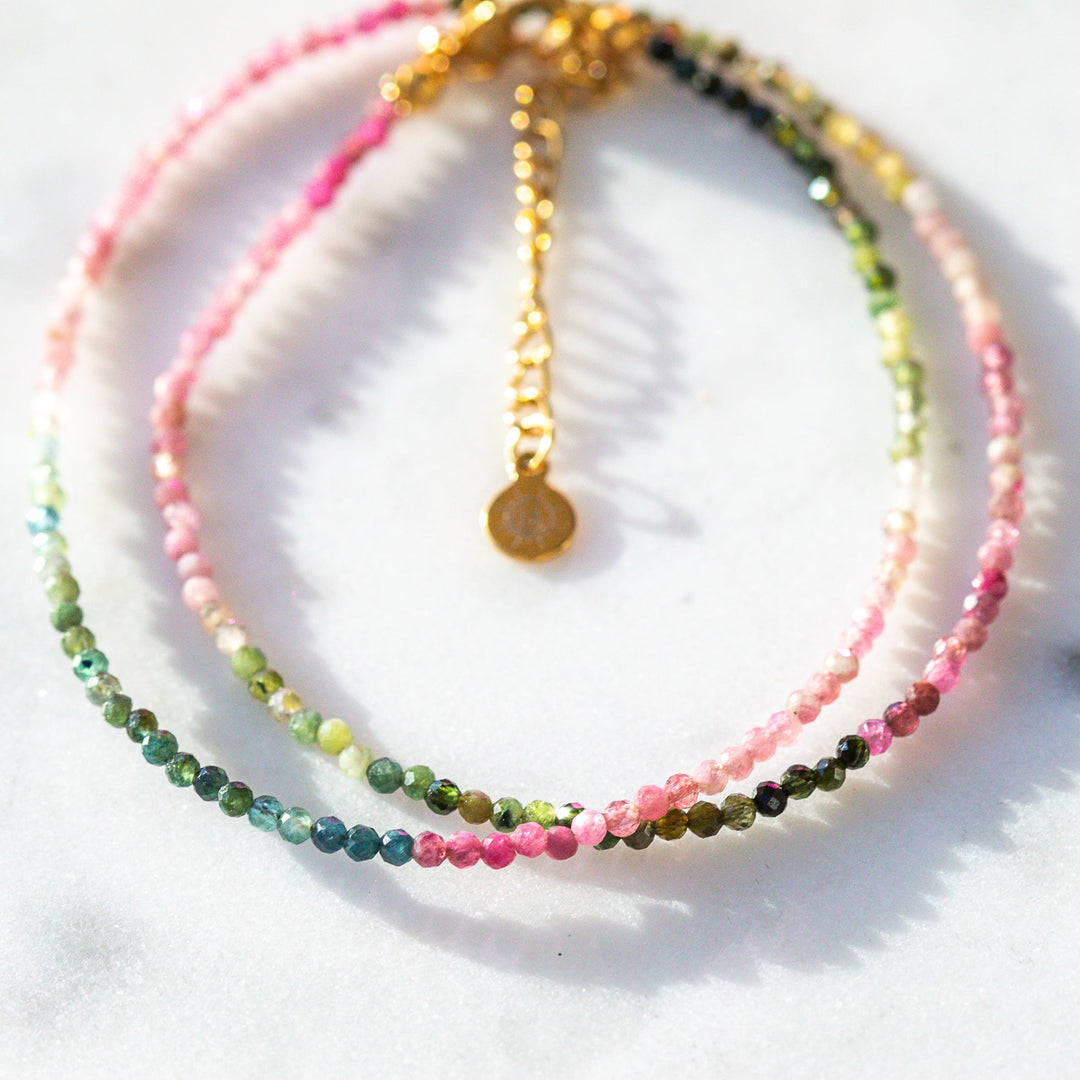 Set of beaded pink green and blue bracelets on a white surface with a leaf shadow