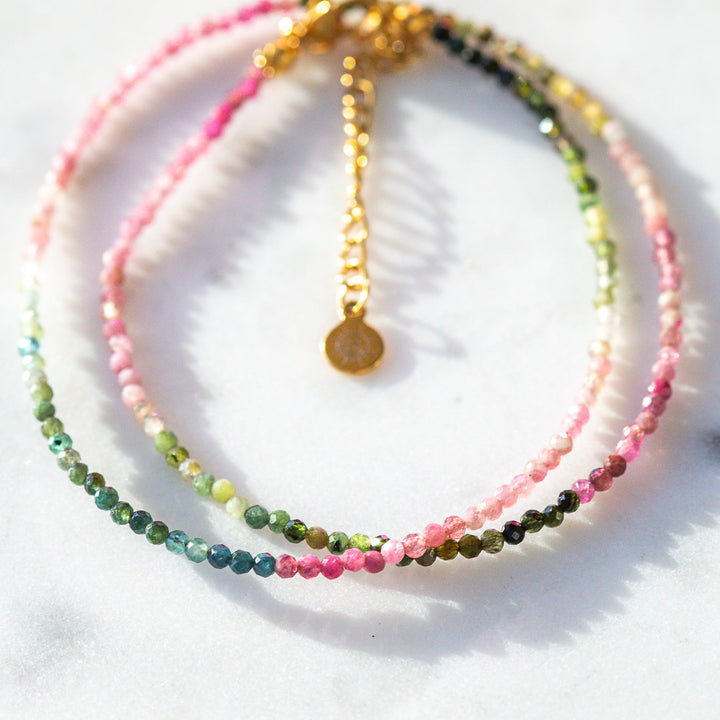 Set of beaded pink green and blue bracelets on a white surface with a leaf shadow