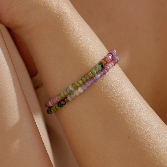 Multicolored healing crystal tourmaline beaded bracelet on a wrist with a blurred background