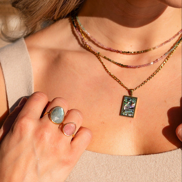 Close-up of a person wearing multiple watermelon tourmaline necklaces, rings, and bracelets with a blurred background. Waterproof necklace 
