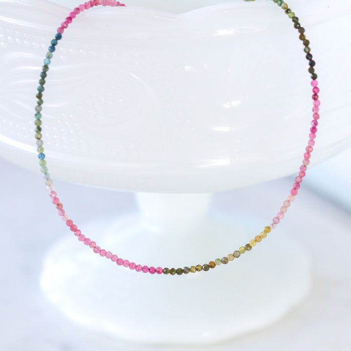 Multicolored dainty beaded gemstone necklace on a white stand
