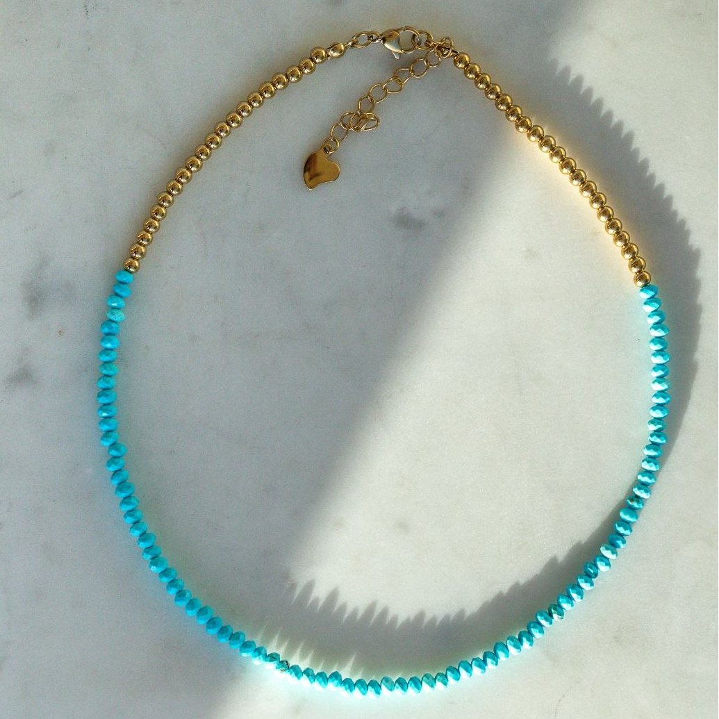 Necklace with blue beads and gold chain on a marble surface