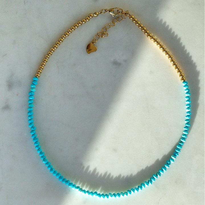 Necklace with blue beads and gold chain on a marble surface